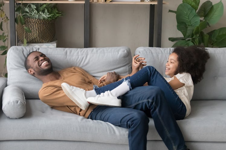 A father and daughter laugh and smile on the couch.