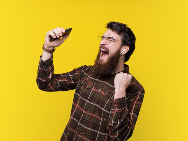 Handsome bearded hipster, excited listening music and gesturing over yellow background
