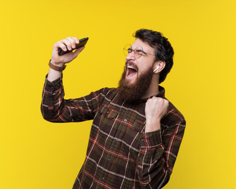 Handsome bearded hipster, excited listening music and gesturing over yellow background