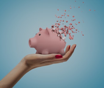 Close-up of woman's hand facing up and holding cute pink piggy bank that has started to disintegrate...
