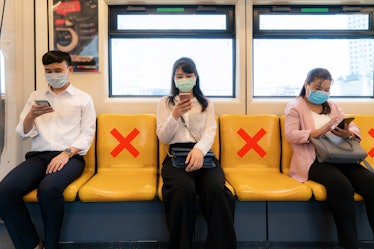 Three Asian people wearing mask sitting in subway distance for one seat from other people keep dista...