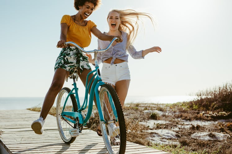 Two happy friends try riding a bike on the walkway to the beach.