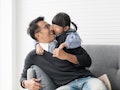 An Asian father and daughter laugh while snuggling on the couch in their living room.