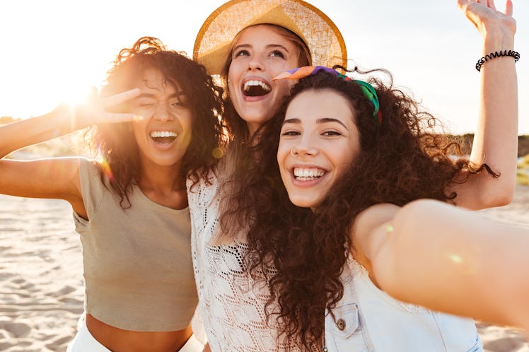 Three happy friends pose for selfie on the beach during the summer.