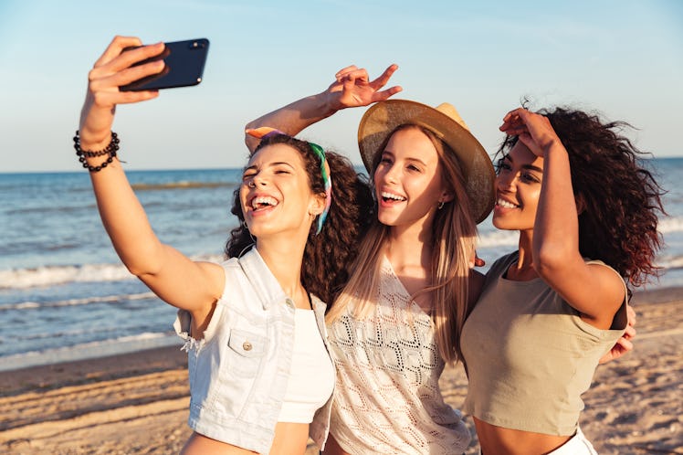 Three happy girls friends in summer clothes taking a selfie at the beach
