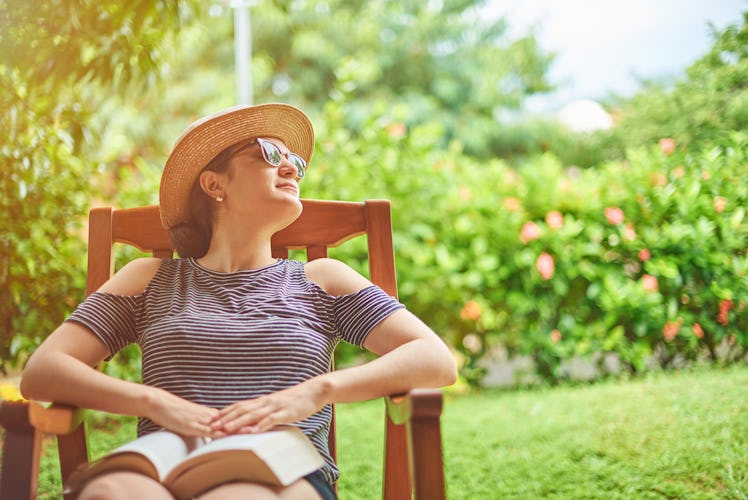 Young woman with book sitting on chair in green garden terrace