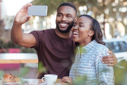 Laughing young African couple taking a selfie together at a sidewalk cafe table while out on a date