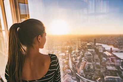 Europe travel woman looking at sunset view of London city skyline from the window of highrise skyscr...