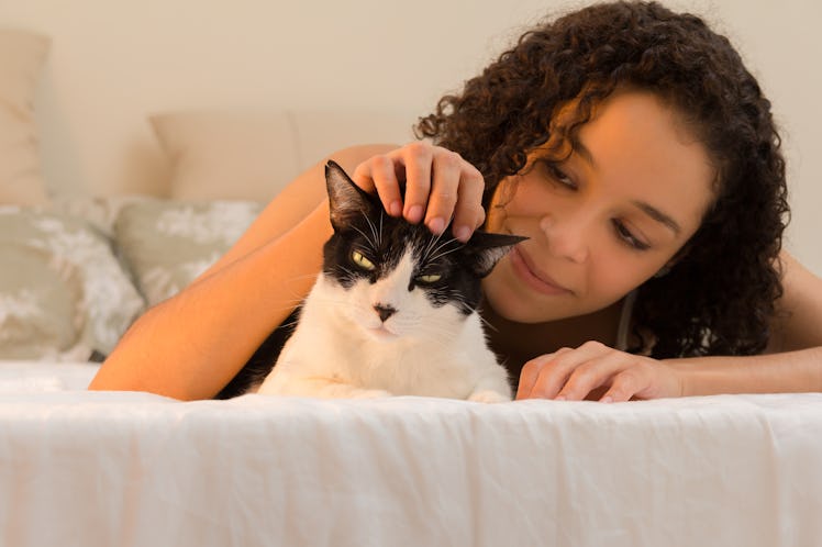 A woman laying in bed, pets her black and white cat on the head. 