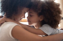 Close up head shot side view calm happy mixed race mother cuddling little cute daughter, touching fo...