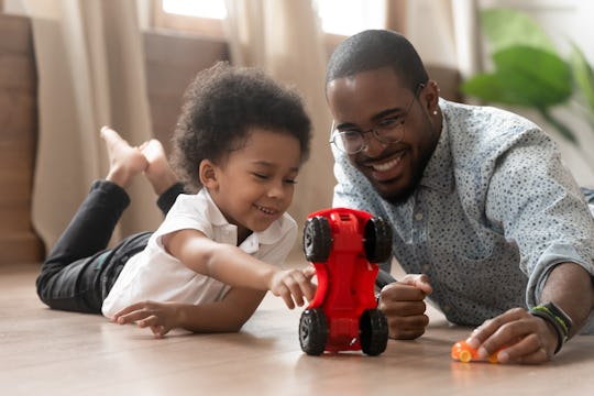 Cute little african kid son play toy cars with black dad, happy family small mixed race son and loving young father babysitter having fun racing on warm floor at home, family daddy child leisure game