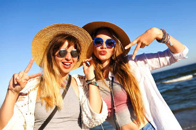 Two best friends throw up peace signs on the beach, while wearing friendship bracelets.