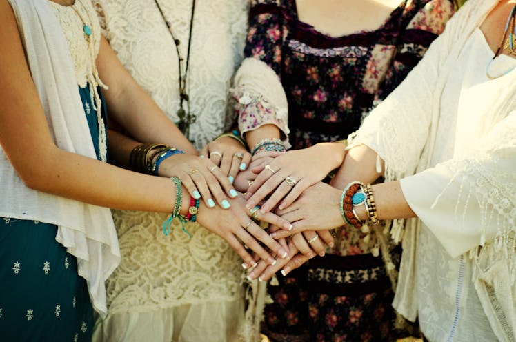 A group of woman wearing boho outfits and friendship bracelets form a circle and join their hands to...
