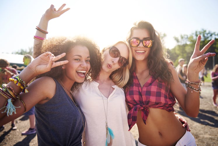 Three happy best friends, wearing friendship bracelets, hang out outside at the festival.
