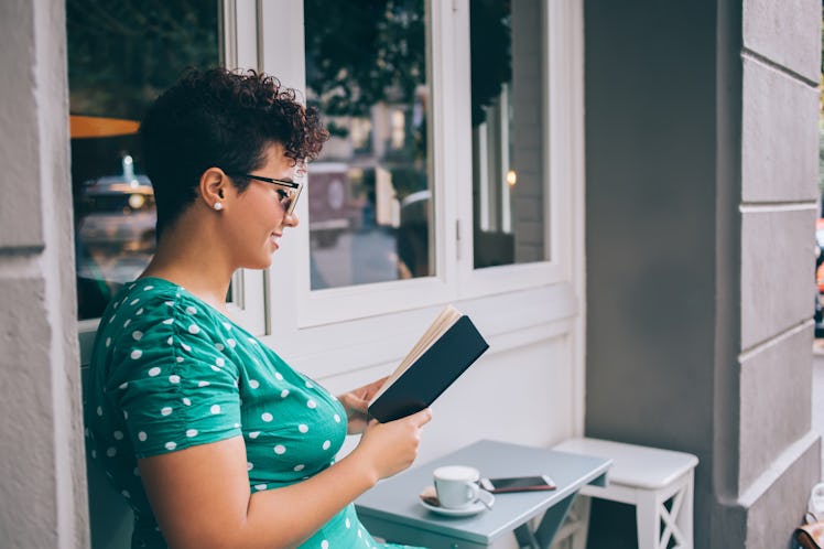 Side view of happy woman in glasses interested on literature plot during leisure time in street cafe...