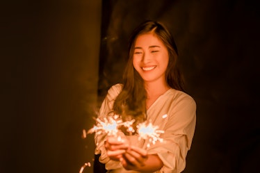 Asian woman holding bright festive Christmas sparkler in hand,firework pyrotechnics and bokeh on the...