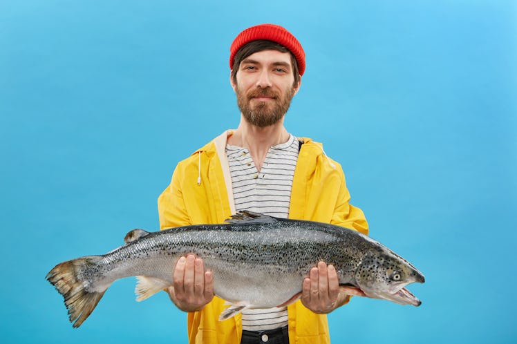Proud bearded fisherman having glad expression catching big fish having successful day. Handsome mal...