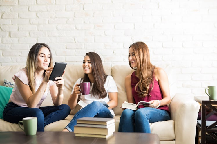 A group of friends in a book club sit on a couch with books and coffee. 