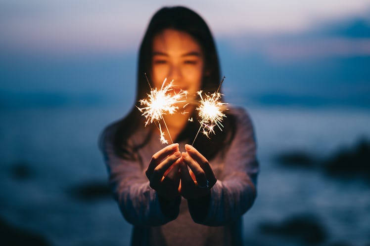 Young happy woman stands on beach with sparkler in sunset light.