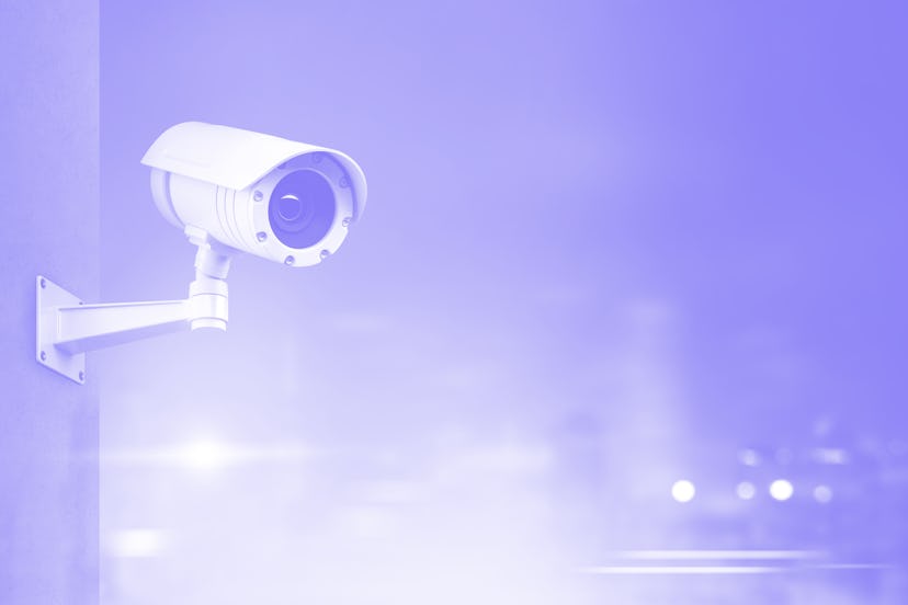 Modern CCTV camera on a wall. A blurred night cityscape background. Concept of surveillance and moni...