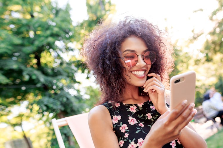 A happy woman with rose-colored sunglasses in her backyard looks at her phone.