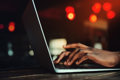 Black man's hands typing on laptop keyboard. Person working with laptop. Beautiful lights as backgro...