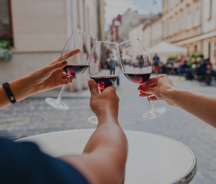 young hipster company of friends sitting in city street cafe, close up hands holding glasses, toasti...