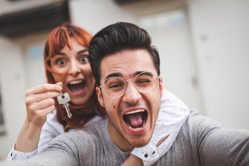 Excited couple with keys to their new home hugging and looking at camera taking selfie