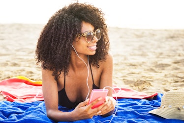 african origin girl relaxing on beach. afro hair woman wearing sunglasses lying on beach using phone...