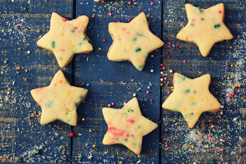 Overhead view of homemade Xmas star sugar cookies with colorful sprinkles on festive blue wooden bac...