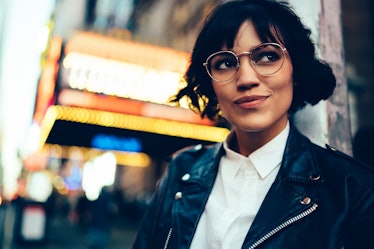 Pretty stylish hipster girl with short haircut looking away walking in New York street with neon lig...