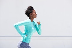 Side portrait of young black woman running outside with earphones