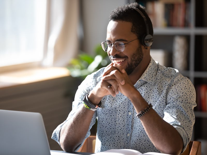 Happy millennial african american man in glasses wearing headphones, enjoying watching educational w...