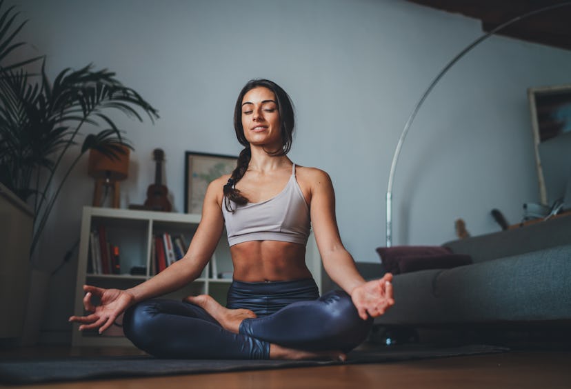 Young healthy beautiful woman in sportive top and leggings practicing yoga at home sitting in lotus ...