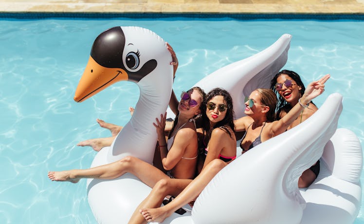 A group of friends sit on an inflatable swan pool float in the pool during the summer. 