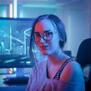 Portrait of the Beautiful Young Pro Gamer Girl Sitting at Her Personal Computer and Looks into Camer...