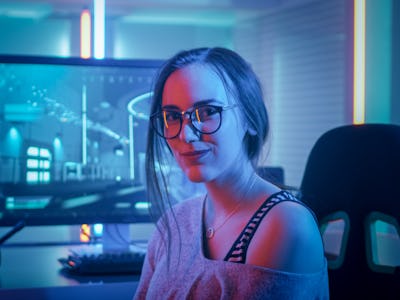 Portrait of the Beautiful Young Pro Gamer Girl Sitting at Her Personal Computer and Looks into Camer...