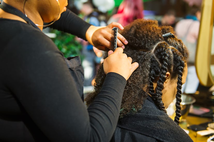 African hairstylist braiding hair of afro American female client in the barber salon.