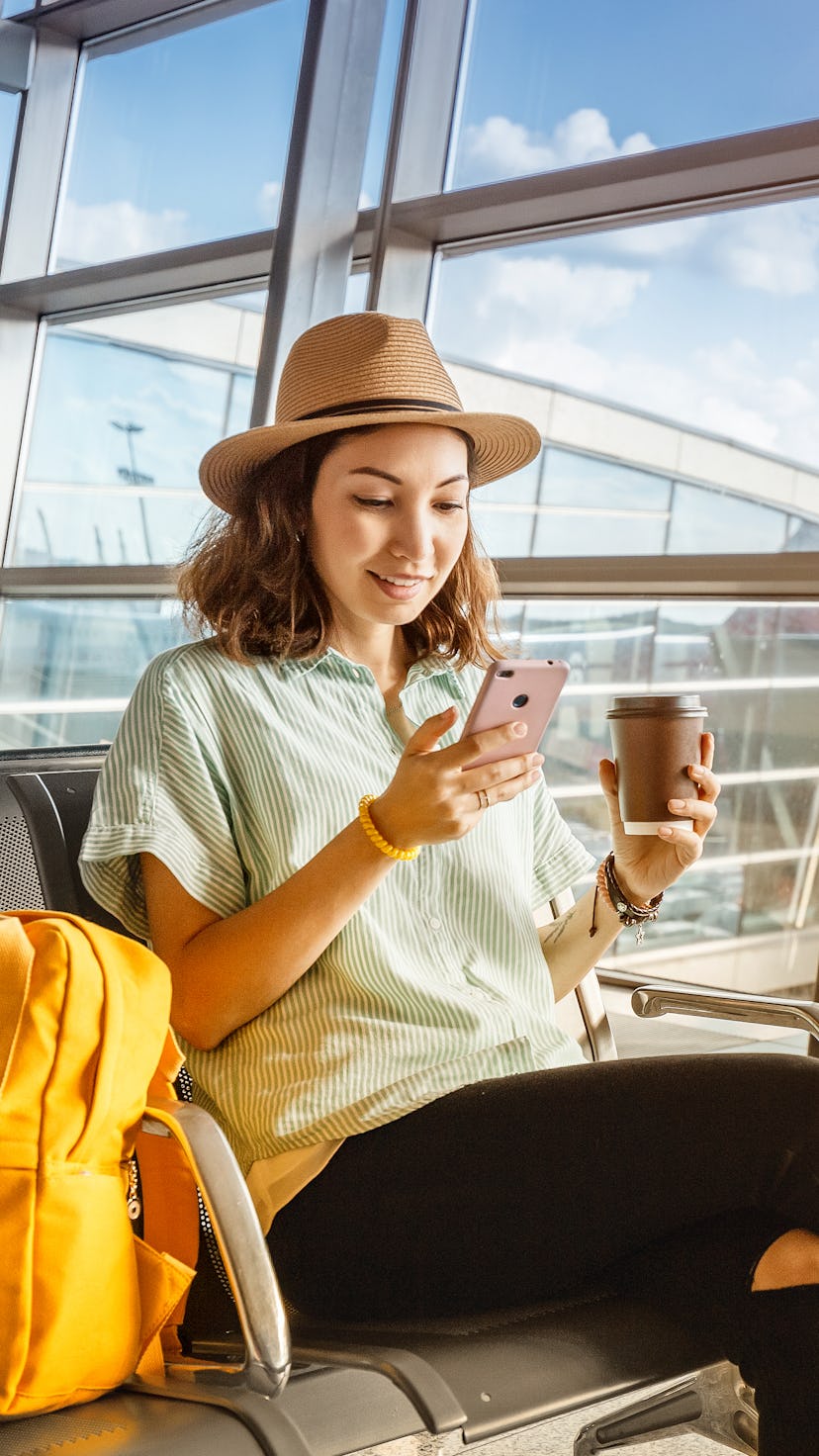 Asian girl waiting for departure at the airport on your vacation. Uses a smartphone and drinks coffe...