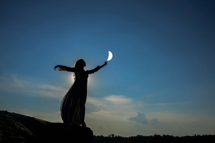 silhoutee of woman standing on top of mountain.  female hold in hand  growing moon above forest tree...