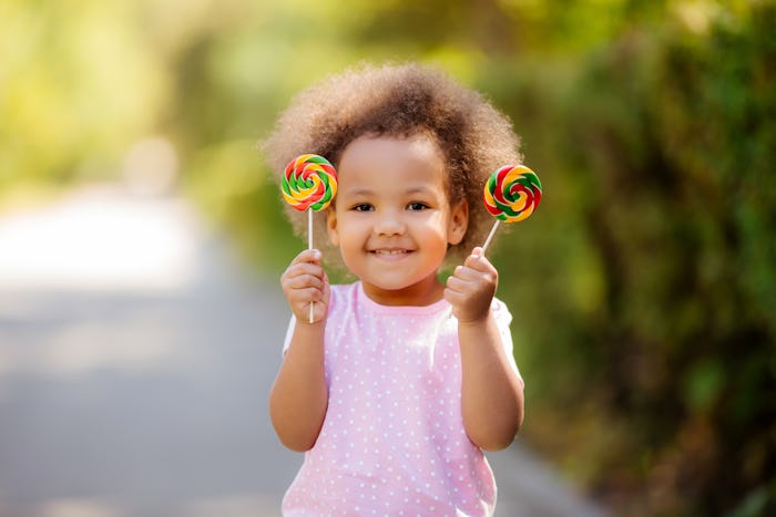 little African American girl in the summer on a walk smiling holding colorful candies