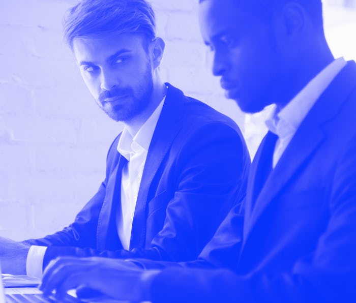 Suspicious cunning male Caucasian worker looking at serious working African American colleague, feel...