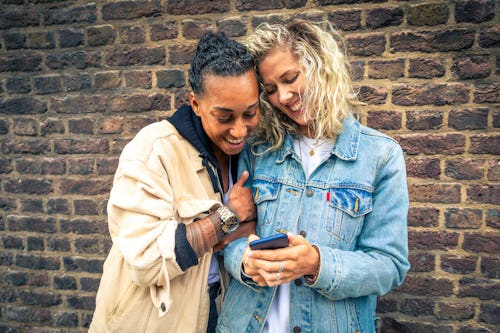 Happy girlfriends looking at a smartphone and having fun - Multiracial lesbian couple, millennials w...