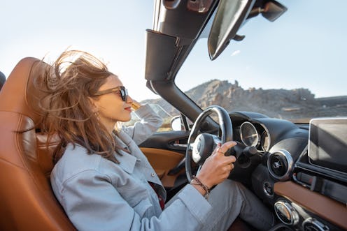 Happy woman driving convertible car while traveling on the desert road. Carefree lifestyle and trave...