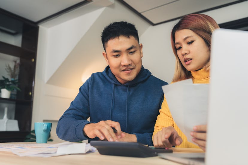 Young asian couple managing finances, reviewing their bank accounts using laptop computer and calcul...