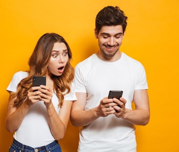 Image of young woman spying and peeking at smartphone of her boyfriend isolated over yellow backgrou...
