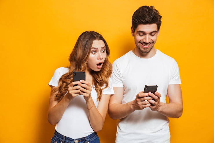 Image of young woman spying and peeking at smartphone of her boyfriend isolated over yellow backgrou...