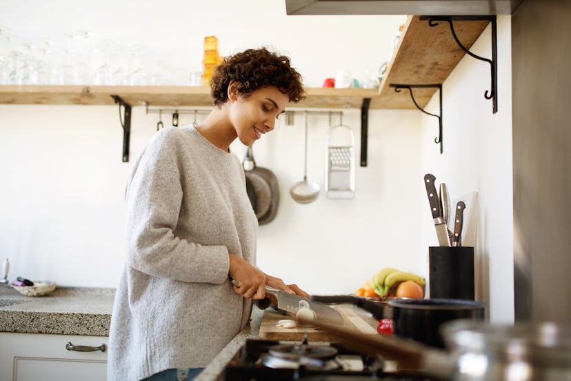 Side portrait of young woman cutting vegetables with knife in kitchen