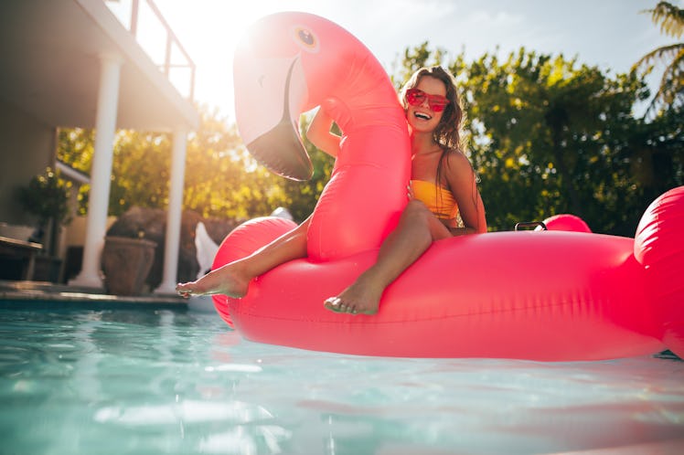 A happy girl with pink sunglasses sits on a flamingo pool inflatable during the summer.