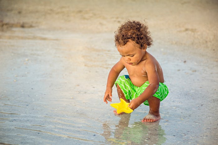 Cute mixed race little boy playing in the sand on a tropical beach vacation. Candid, Full length pho...
